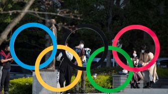 People wearing masks stand near the iconic Olympic rings in Tokyo, Japan.