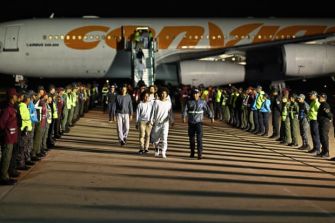 Venezuelan migrants disembarking from an aircraft, accompanied by airport personnel and security, highlighting the deportation process.