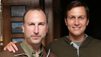 Two men standing close together, one wearing a jacket and the other dressed in a hoodie.