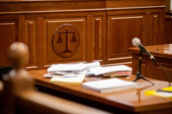 A courtroom interior with a wooden bench, scattered papers, and a microphone, featuring a symbol of justice.