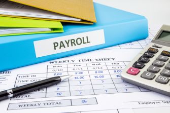 A close-up view of payroll documents, including a weekly time sheet and a calculator, highlighting issues related to a payroll system switch.