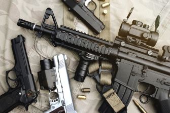 An assortment of firearms, including handguns and an assault rifle, displayed on a surface with ammunition.