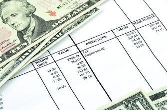 A close-up view of a payroll document alongside U.S. dollar bills.