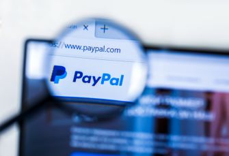 Close-up of a magnifying glass over a computer screen displaying the PayPal logo and the URL www.paypal.com.