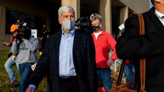 Former Michigan Governor Rick Snyder surrounded by media, leaving a building related to charges in the Flint water crisis.