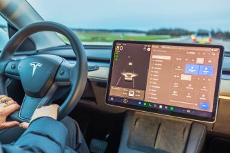 Interior view of a Tesla vehicle showing the steering wheel and dashboard display with driver assistance features activated.