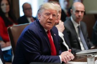 Donald Trump seated at a meeting table, addressing attendees.