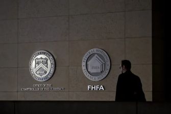 A person walking past the logos of the Office of the Comptroller of the Currency (OCC) and the Federal Housing Finance Agency (FHFA) on a wall.