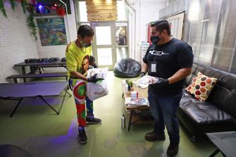 Two individuals interact in a safe-injection site, with one person receiving supplies from a staff member while seated in a relaxed, supportive environment.