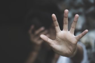 A hand raised in a gesture of stopping or protecting, with a blurred figure in the background showing signs of distress.