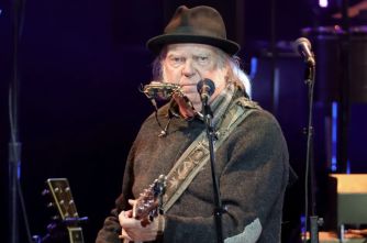 Neil Young performing on stage with a harmonica and guitar.