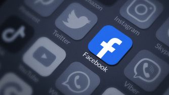 An image of a smartphone screen displaying various app icons, with the Facebook app prominently featured in blue.