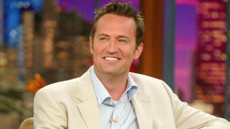 A smiling man in a light suit during a television interview.