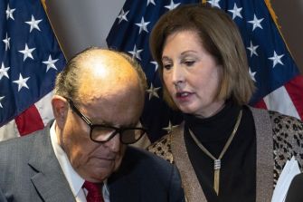 Sidney Powell speaking with Rudy Giuliani in front of American flags.