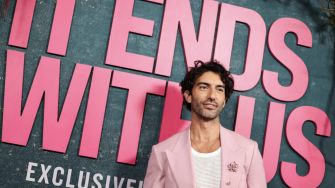 Actor posing at the premiere of the film "It Ends With Us," featuring a pink backdrop with the movie's title.