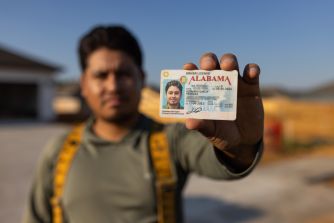 A person holding an Alabama driver's license while standing at a construction site.
