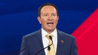 A man in a suit speaking into a microphone against a colorful background.