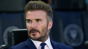 David Beckham in a formal setting, wearing a suit and sitting in a sports environment.