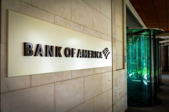 Exterior of a Bank of America branch with a large sign on a stone wall and a glass revolving door.