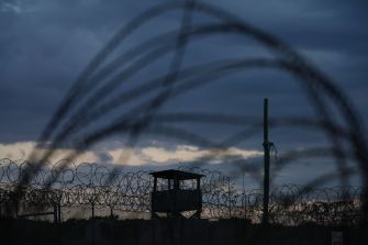 Silhouette of barbed-wire fencing and a guard tower at Guantanamo Bay detention camp at dusk.