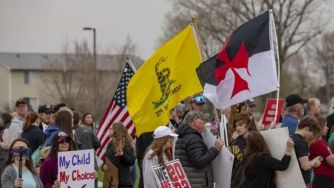 A group of protesters holding signs and flags during a demonstration related to school policies in Iowa.