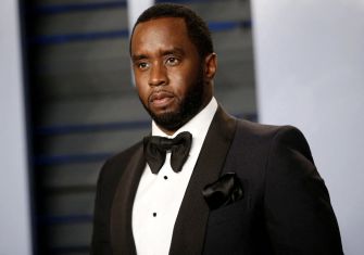 A man in a tuxedo with a serious expression, standing against a blurred background.
