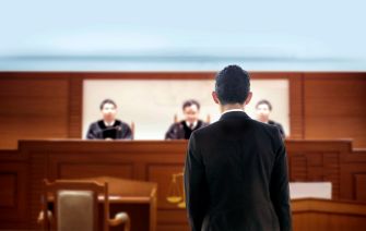 A defendant standing in a courtroom facing three judges.