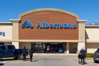 Exterior of an Albertsons grocery store with a large blue sign on a wood-paneled facade and a clear blue sky.