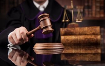 A judge's gavel on a sounding block with legal books in the background.