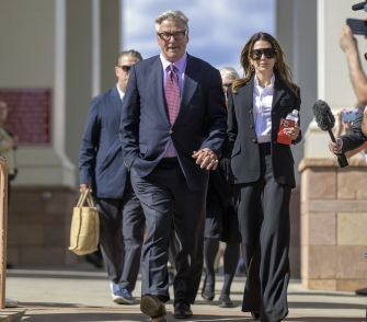 Alec Baldwin and a woman walking outside, surrounded by other individuals, following a court appearance.