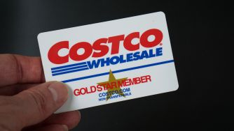 Close-up of a Costco Gold Star membership card held by a hand against a dark background.