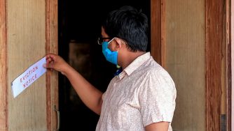 A person wearing a mask reading an eviction notice while standing at a doorway.