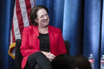 Justice Elena Kagan speaking at a judicial conference, advocating for an enforceable code of conduct for Supreme Court justices, with an American flag in the background.