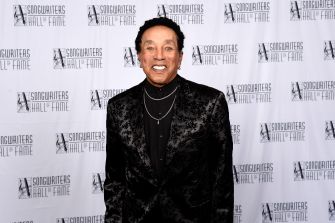 Smiling man in a black patterned suit posing on a red carpet with Songwriters Hall of Fame logos behind him