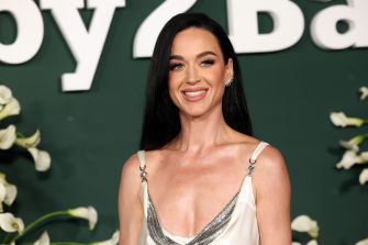 Smiling woman with long dark hair wearing a pale sleeveless dress at a media event.